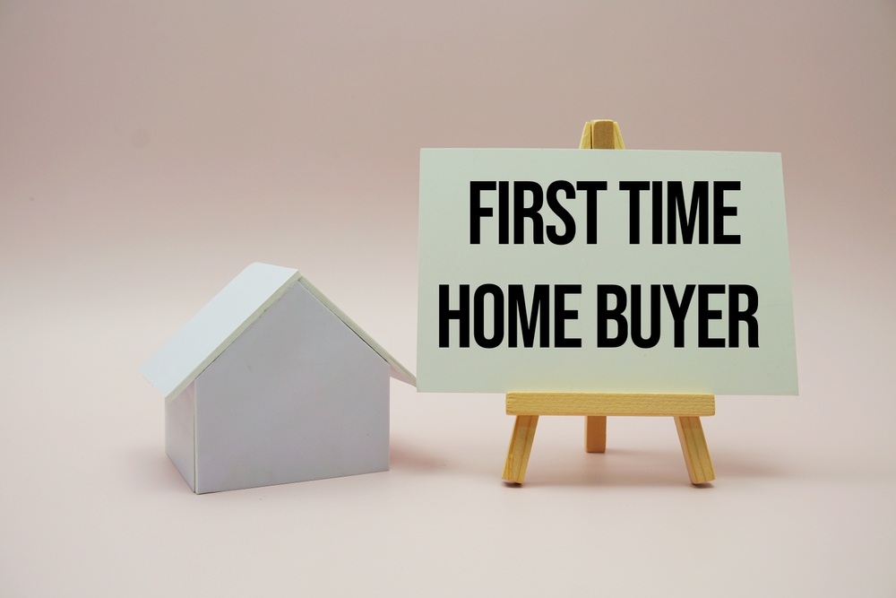Image of a small model house with a display board on an easel displaying a seminar for first-time buyers